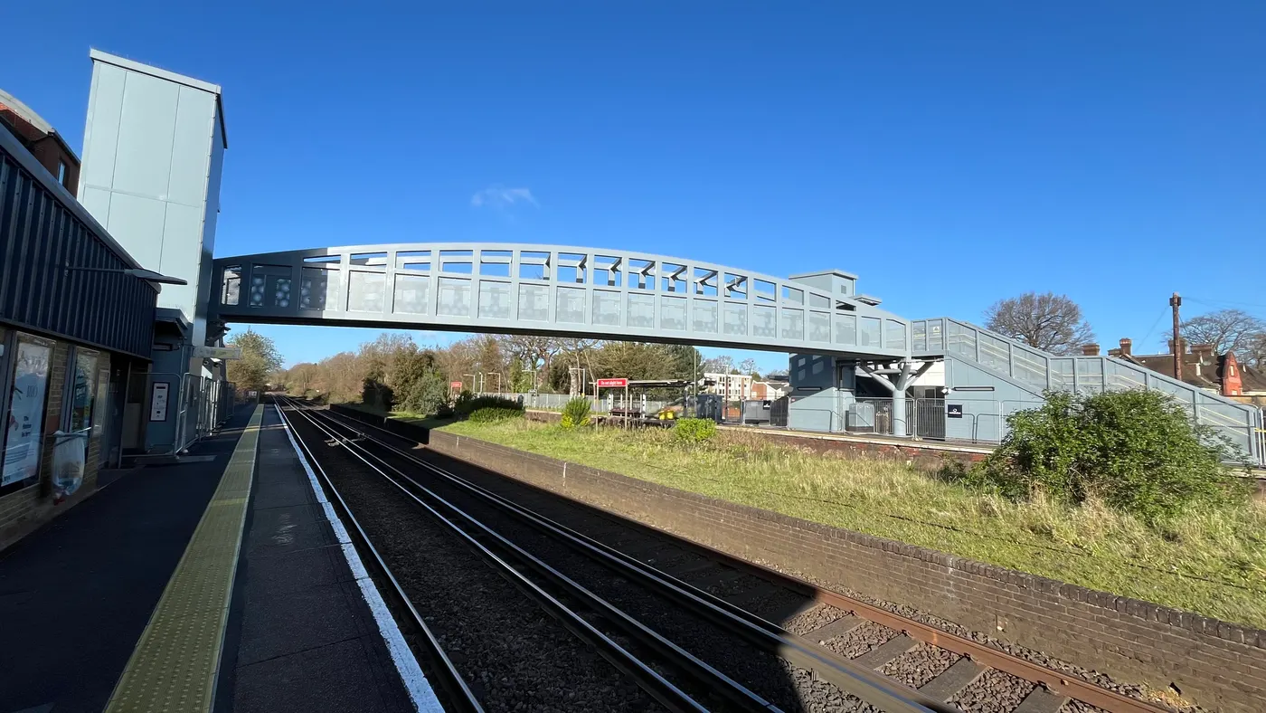The arched steel footbridge at Walton-on-Thames station spanning the four tracks, with a lift tower at each end and a platform running below it
