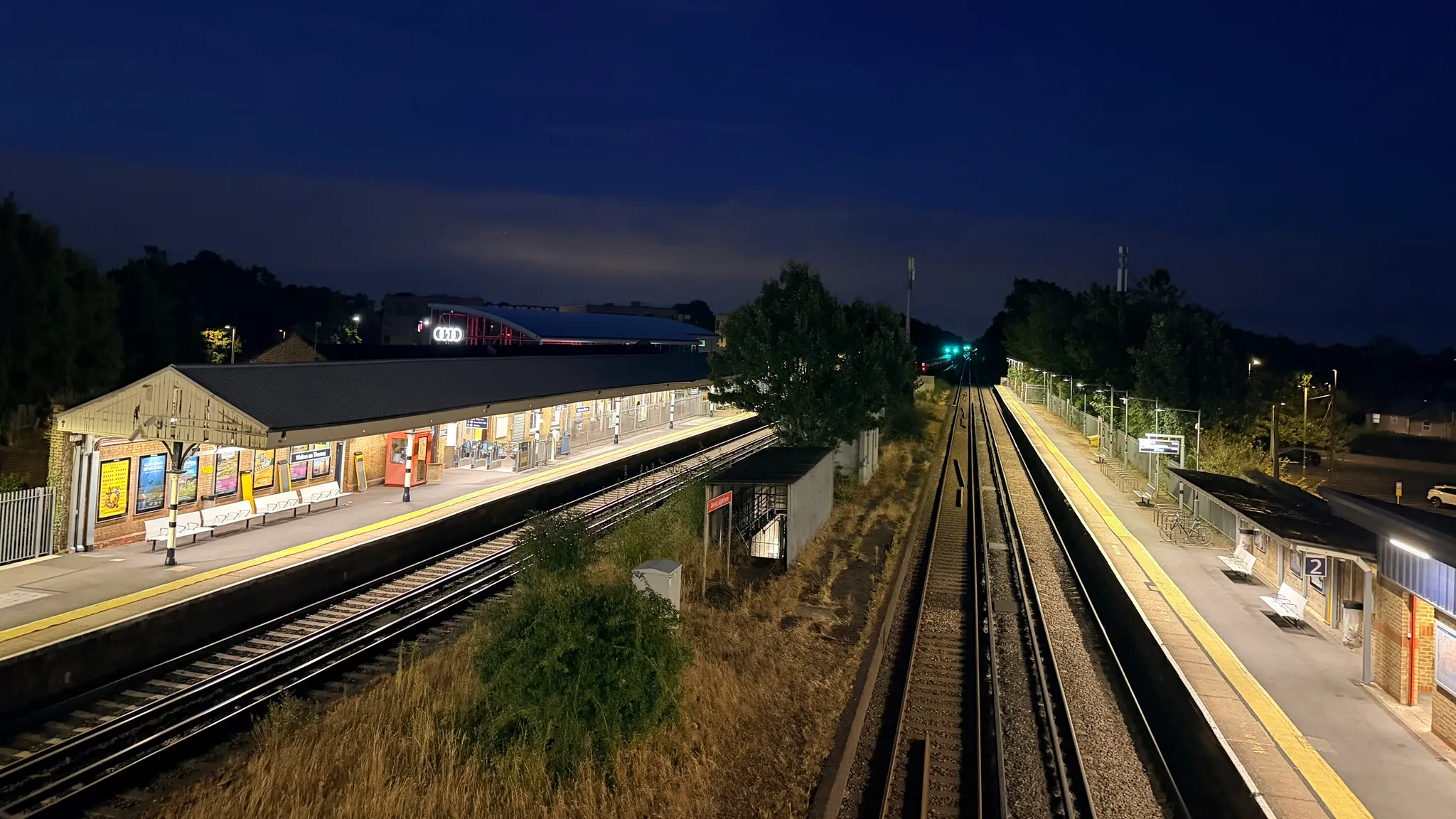 Walton-on-Thames railway station at night seen from the footbridge, with Platform 1 lit on the left, the central fast lines and disused platforms in the middle, and Platform 2 on the right