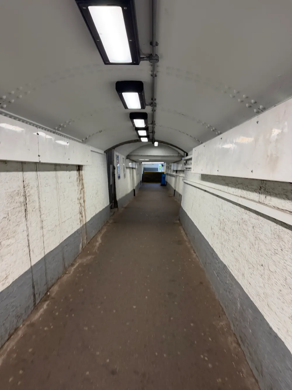 The older pedestrian subway at Walton-on-Thames station: a long, low, white-painted tunnel with a curved ceiling and strip lighting, ending in a flight of steps